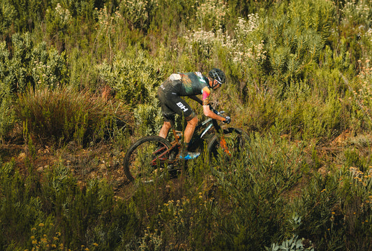 Corredor del BH Coloma Team, con maillot de Gobik, atravesando una zona con abundante vegetación en una etapa de la carrera.